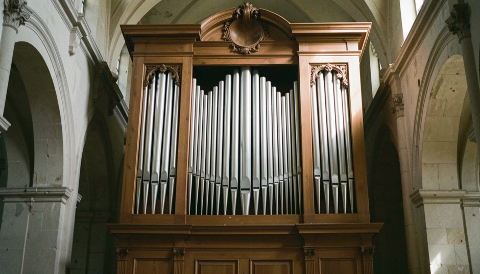 Facciata di un organo storico con canne di stagno allineate per altezza dentro una cornice lignea, penombra di chiesa e luce laterale
